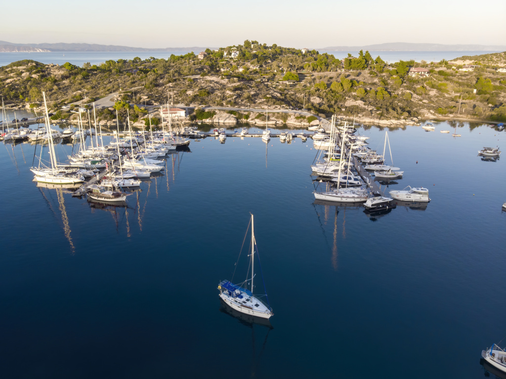 aegean-sea-port-with-multiple-moored-yachts-near-piers-greenery-blue-water-view-from-drone-greece.jpg